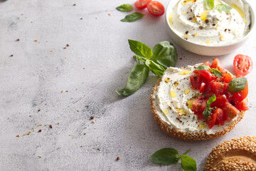 Fresh bun with sesame seeds with cheese cream and fresh tomatoes with basil leaves copy space
