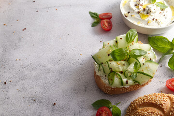 Fresh bun with sesame seeds with cheese cream and fresh cucumbers with basil leaves copy space