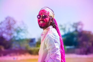 Young indian man with sunglasses play holi festival with his face painted with powder color or...