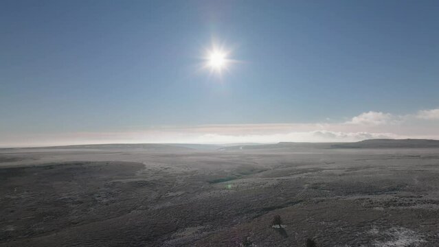 A low winter sun and blue sky over a large frozen moorland, snowy tundra to the horizon.