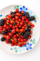 Fresh berries on a plate on a white background, red and black currants and black mulberries, wild strawberries and cherries, top view