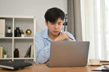 Serious businessman watching online presentation on laptop computer during working remote from home