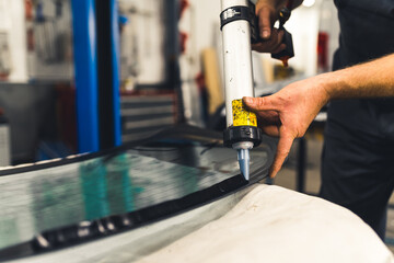 Worker applying an adhesive sealant to car windscreen preparing for replacement. High-quality photo.