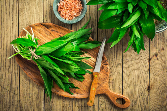 Fresh wild leek leaves on a wooden board. Leaves of fresh ramson with pink Himalayan salt