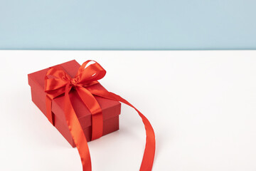 Red gift box with a red satin ribbon on the table and a blue background.