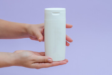 Woman holds a white bottle (cream, lotion, gel, shampoo) for cosmetic products isolated on lilac background
