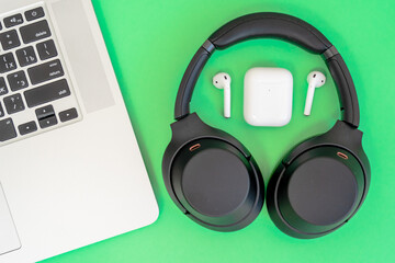 Laptop with big and small wireless headphones on green background