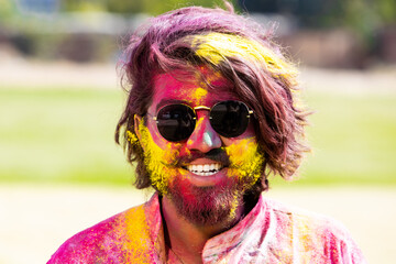 Portrait of happy Indian man wearing sunglasses and painted face celebrating Holi festival with...