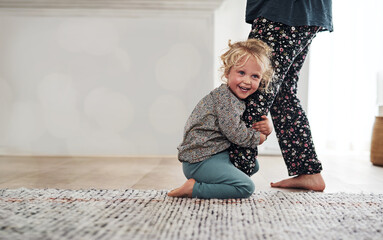 Happy, child clinging to leg of woman and playful fun and smile on carpet in home with mother....