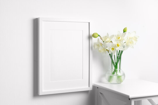 Blank art frame mockup on white wall with flowers bouquet