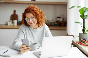Portrait of smm specialist working from home at kitchen table, looking at smartphone screen,...