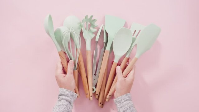 Flat lay. New blue silicone kitchen utensils with wooden handles on a pink background.