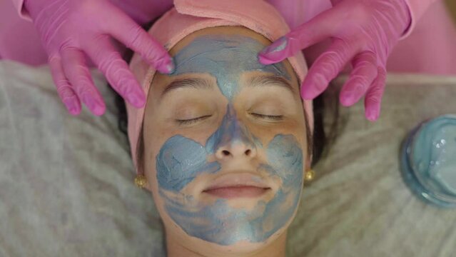 Close-up shot of a woman enjoying facial treatment with clay mask at beauty shop. Cosmetology and spa
