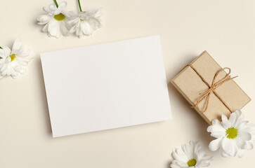 Blank greeting card mockup with gift box and white daisy flowers, top view with copy space