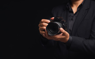 Photographer in a suit holding the digital camera while standing on a black background - Powered by Adobe