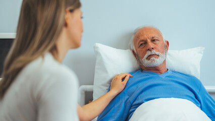 Fototapeta premium In the Hospital Ward Recovering Father is Visited by Daughter. Senior Sick Man Sleeping in Bed Daughter Sits Beside, Worrying. Modern Private Ward. Family Values. 