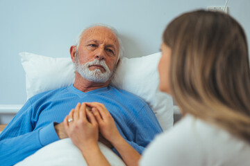 Obraz premium Hospital visit from the family daughter for sick senior. In the Hospital Ward Recovering Father is Visited by Daughter. Senior Sick Man Sleeping in Bed Daughter Sits Beside, Worrying. 
