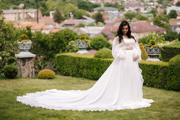 Elegant pregnant woman in beautiful white dress walking outdoors