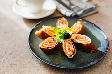 Delicious thin pancakes withsmoked salmon and cream cheese on light wooden table. Morning breakfast concept