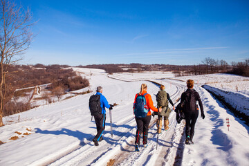 Rear view a group of people hiking on winters trail. Rural road covered by snow. Winter adventure journey. Winter nature landscape.	