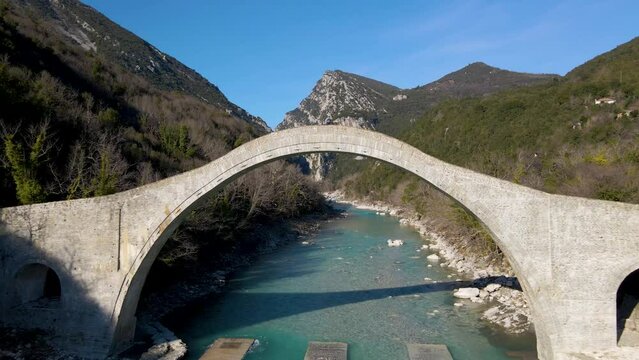 Flying backwards under a huge arched stone bridge over a river in Plaka, Tzoumerka, Greece