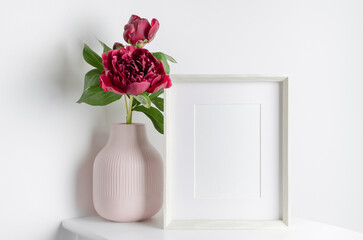 White portrait frame mockup with red peony flowers in vase, blank mockup