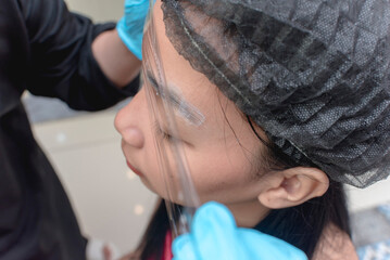 An esthetician wraps numbing preservative film around the clients eyebrow area after anesthetic application prior to a microblading procedure.