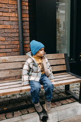 Sad little boy, outdoors, sitting on a wooden bench.