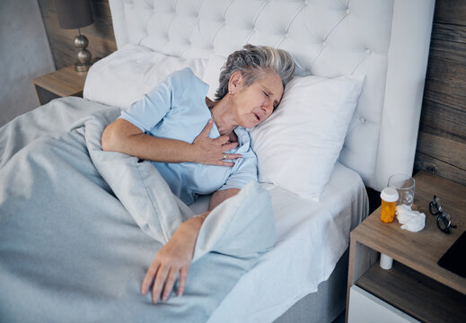 Heart attack, bedroom and senior woman with chest pain, sick and medical risk with medicine. Pills, stress or stoke of elderly person cardiology, breathing or lung problem with healthcare emergency
