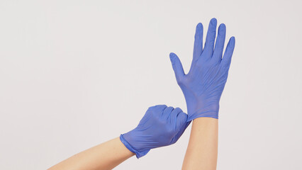 Hand is pulling purple latex gloves on white background.