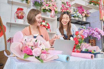 Two young beautiful female florist partners discuss flora bunch decoration, online purchase orders and website arrangement for business, happy work in colorful flower shop store, and e-commerce SME.