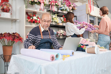 Asian senior male florist owner works with laptop, online selling in e-commerce business website,...