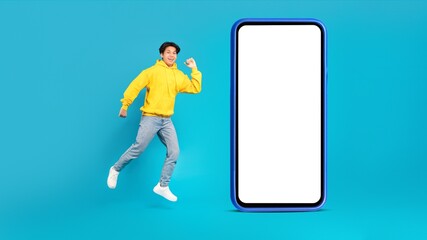 Japanese Teenager Boy Near Large Smartphone Jumping On Blue Background
