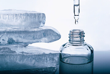 A bottle of face serum and a pipette on the background of pieces of melting ice.