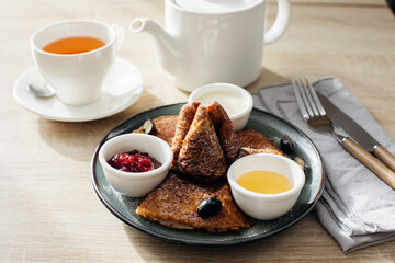 Thin pancakes, russian blini or french crepes with jam, honey and sour cream and cup of tea on light wooden table. Morning breakfast concept