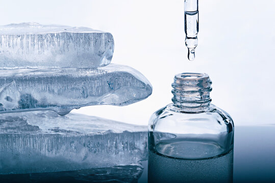 A bottle of face serum and a pipette on the background of pieces of melting ice.