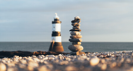 Lighthouse with pebble stack balanced next to it.  Forced perspective.  Calming scene perfect for yoga and mindfulness.  Penmon Lighthouse, Anglesey, Wales. 