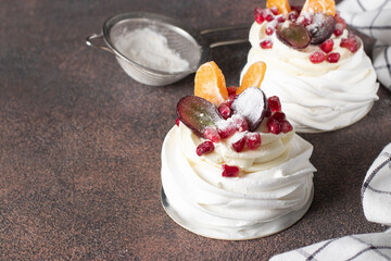 Mini Pavlova cake with pomegranate, tangerines and grapes on brown background