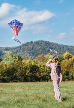Little girl flying a colorful kite on the green grass meadow in the mountain fields. Happy childhood moments or outdoor time spending concept image. 