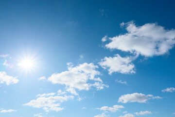 The blue summer sky with white fluffy clouds. Shining sun at clear blue sky with copy space