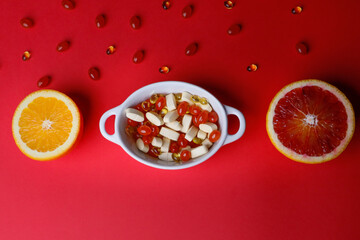 Vitamins pills in a spoon on a red background and citrus fruits