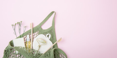 Cosmetic products and hygiene items in a green string bag on a pink background. The concept of sustainable shopping and smart consumption. Self care concept. Copy space