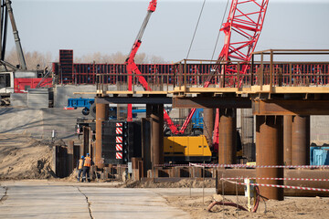 The mobile crane is loading the cargo. View of the construction site with machinery, people at...