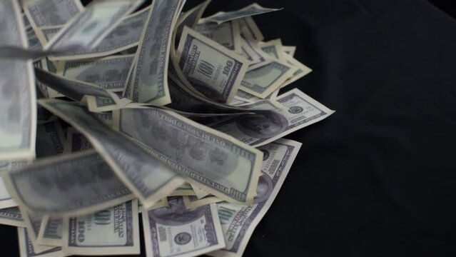 Cash one hundred dollar bills fall on a black background in a pile. Money dollars fall from the top onto the black table forming a big pile. The winnings pour in dollars on the black table.