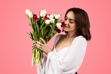 Glad young european woman smelling bouquet of flowers, enjoy lifestyle and aroma of tulips