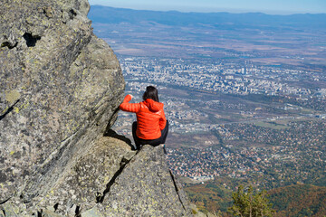 Obraz premium Woman sitting on a rocks high in the autumn mountain above the city of Sofia. Vitosha mountain, ,Bulgaria