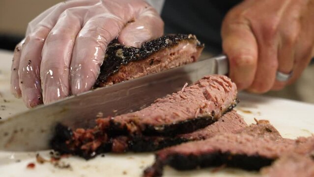 Pitmaster carefully slices tender Texas smoked barbecue beef brisket for plating, slow motion close up 4K