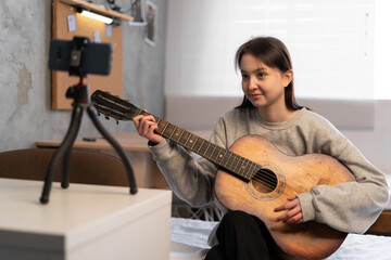 Obraz premium Home blogger concept. Asian female vlog influencer plays guitar performance music and streaming for digital internet online audience listening at home.