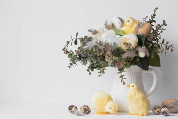 Banner. The concept of a bright Easter holiday. A bouquet of flowers with feathers, yellow chickens and Easter quail eggs on a white isolated background. Beautiful Easter card.
