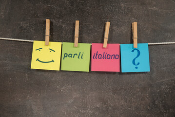 Napis Parli italiano na kolorowych karteczkach wiszących na ciemnym tle - obrazy, fototapety, plakaty